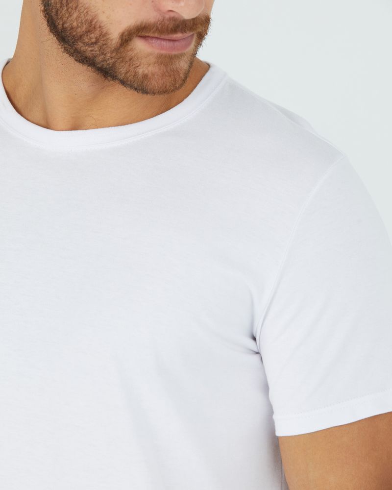 Homem branco com boné marrom e camiseta básica branca masculina com decote redondo e pesponto em algodão e short verde.