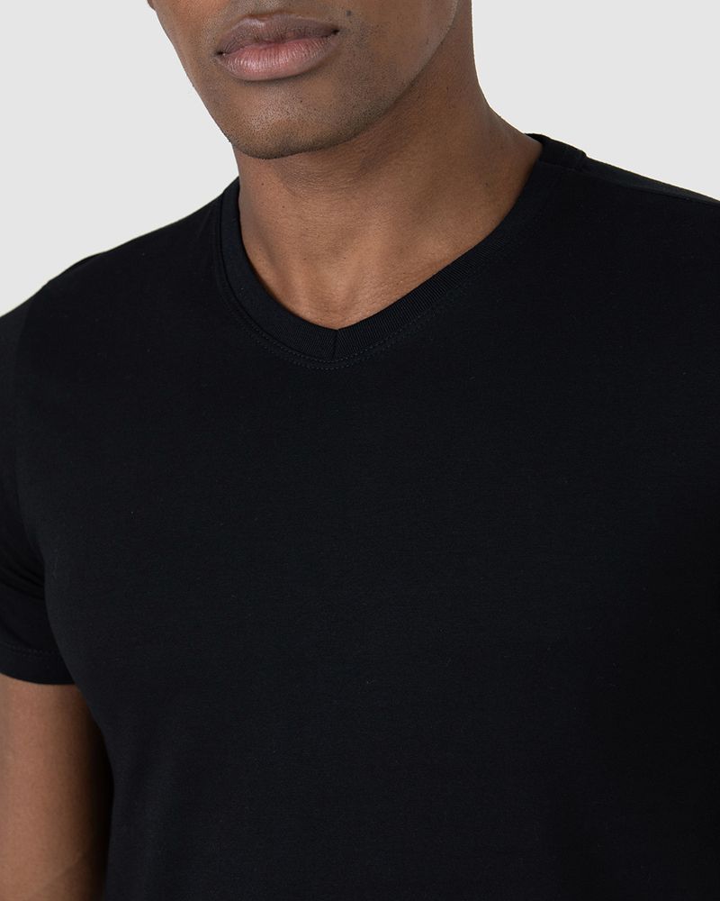 Homem negro cabelo preto e utilizando camiseta básica preta masculina gola V em algodão e calça cinza.