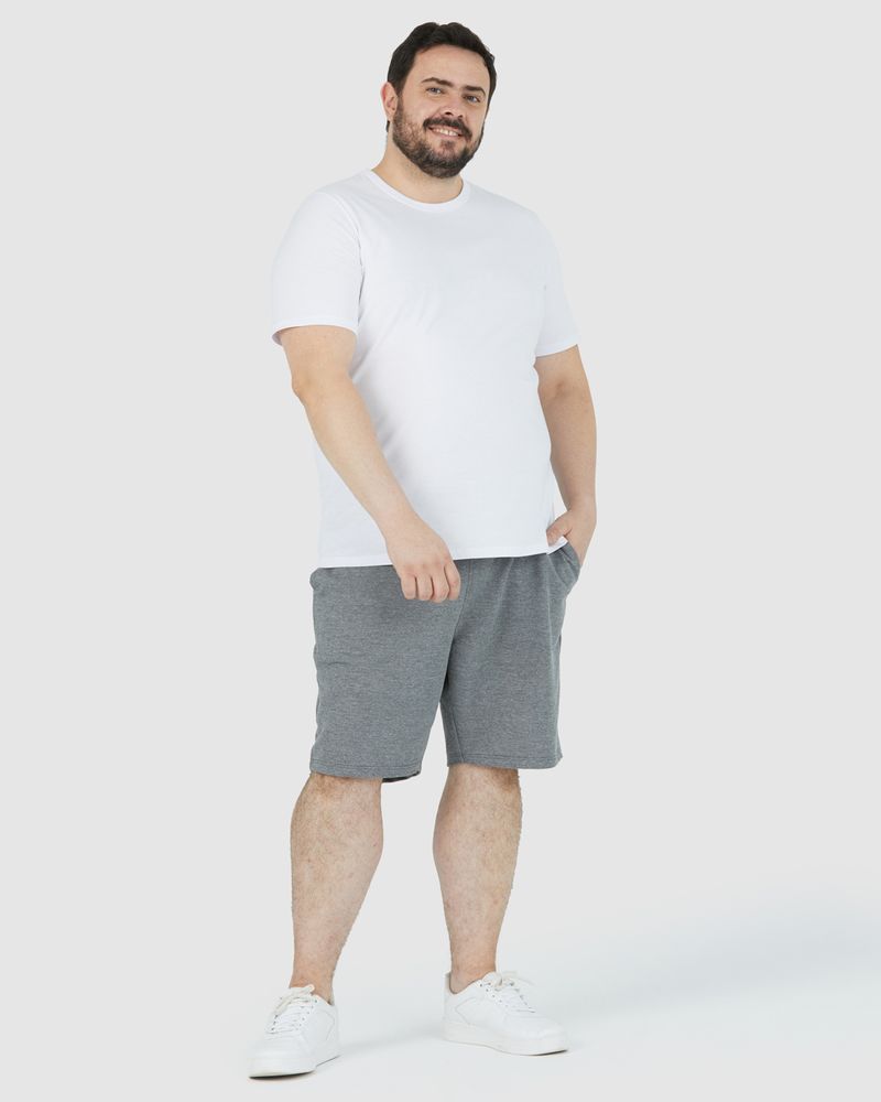 Homem branco de cabelo preto sorrindo e utilizando camiseta básica plus size masculina cor branca com decote redondo em algodão e bermuda cinza.