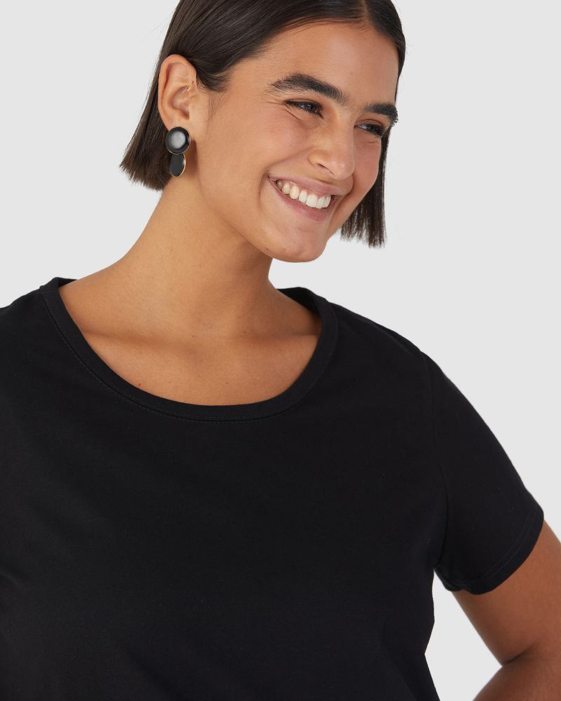 Mulher branca de cabelo curto utilizando blusa básica plus size, cor preta com decote redondo em algodão.