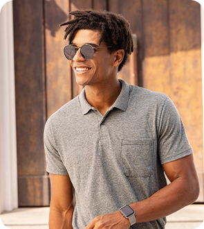Homem negro sorrindo usando óculos de sol e camisa polo básica.